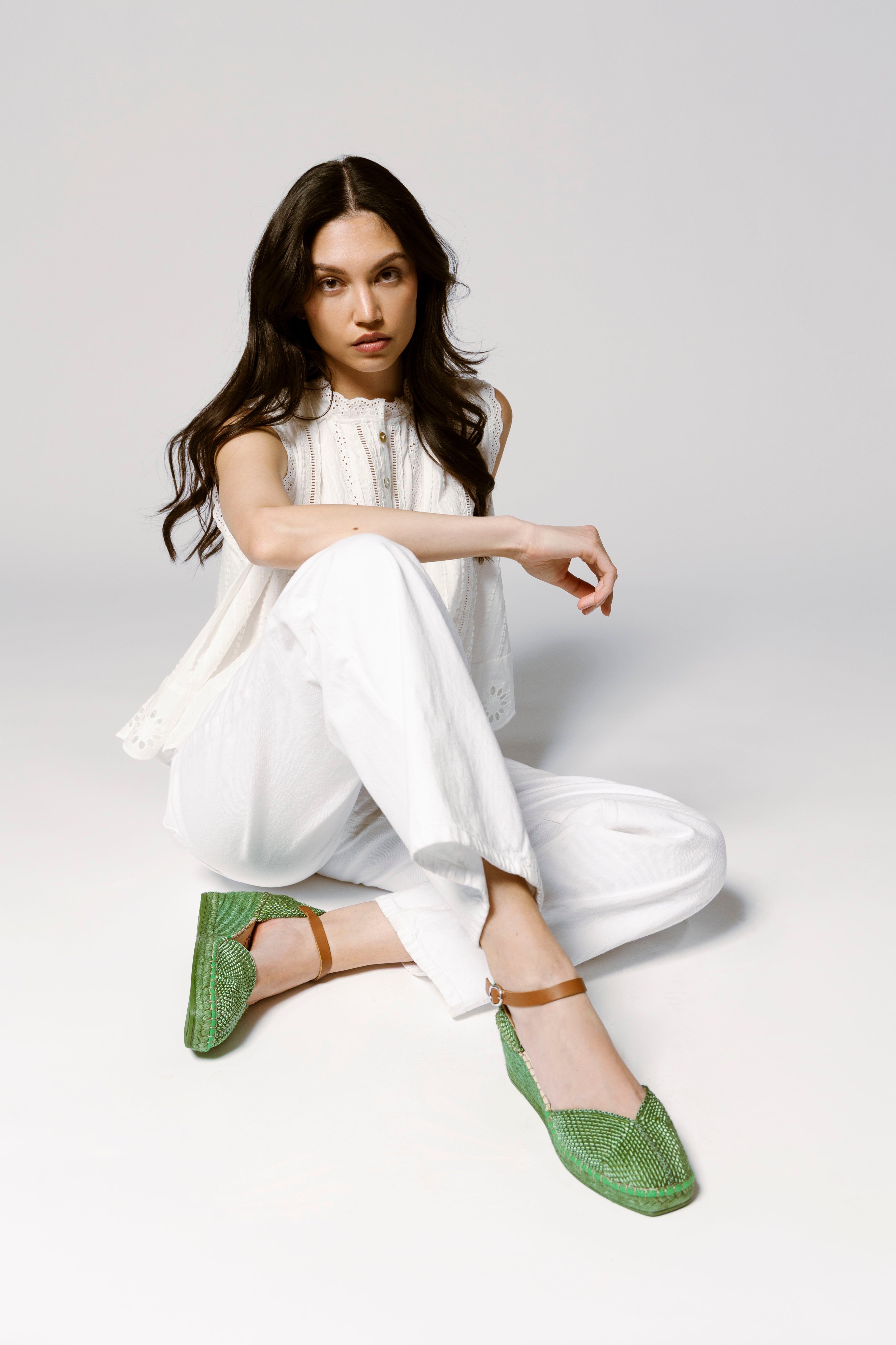 picture of a woman wearing white blouse with white jeans and green espadrilles with a link to shop the back in stock collection